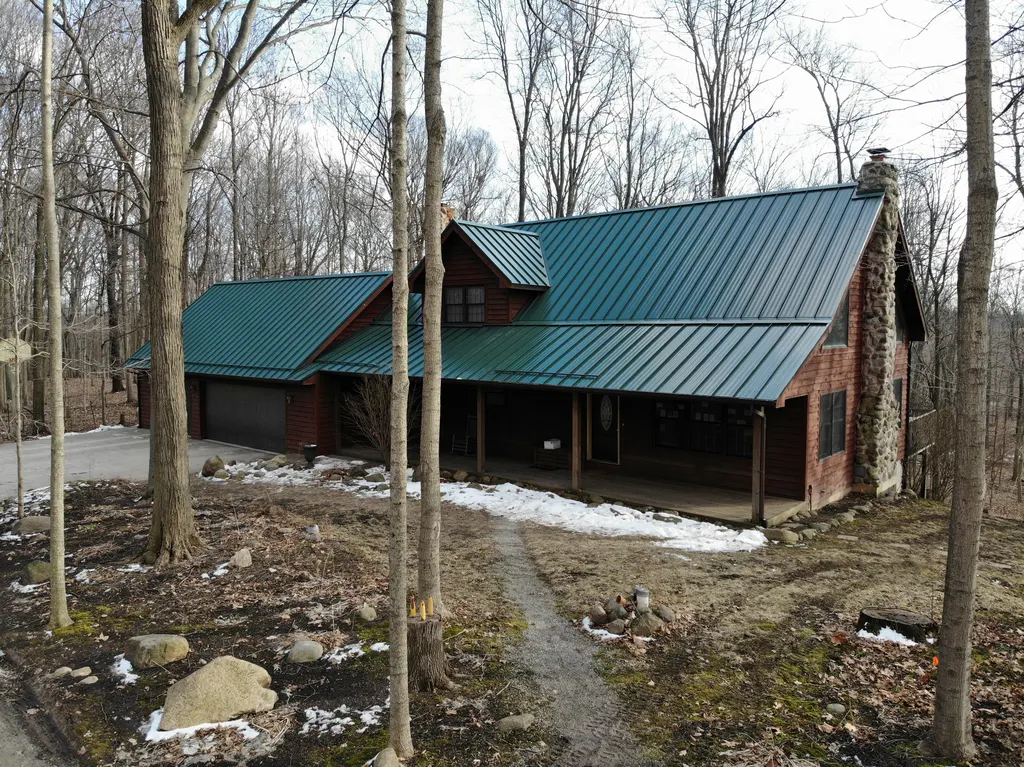 Log home with a green standing-seam metal roof among bare winter trees