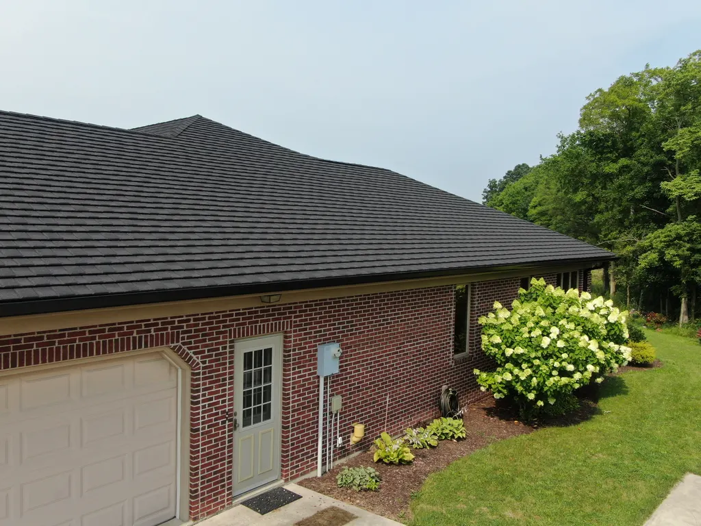 Close aerial view of a red brick home's black stone-coated shake metal roof